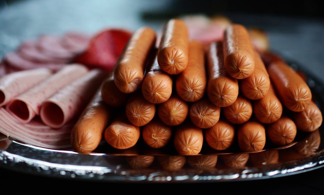 Delicious assortment of hot dogs and sliced meats artfully arranged on a silver platter.