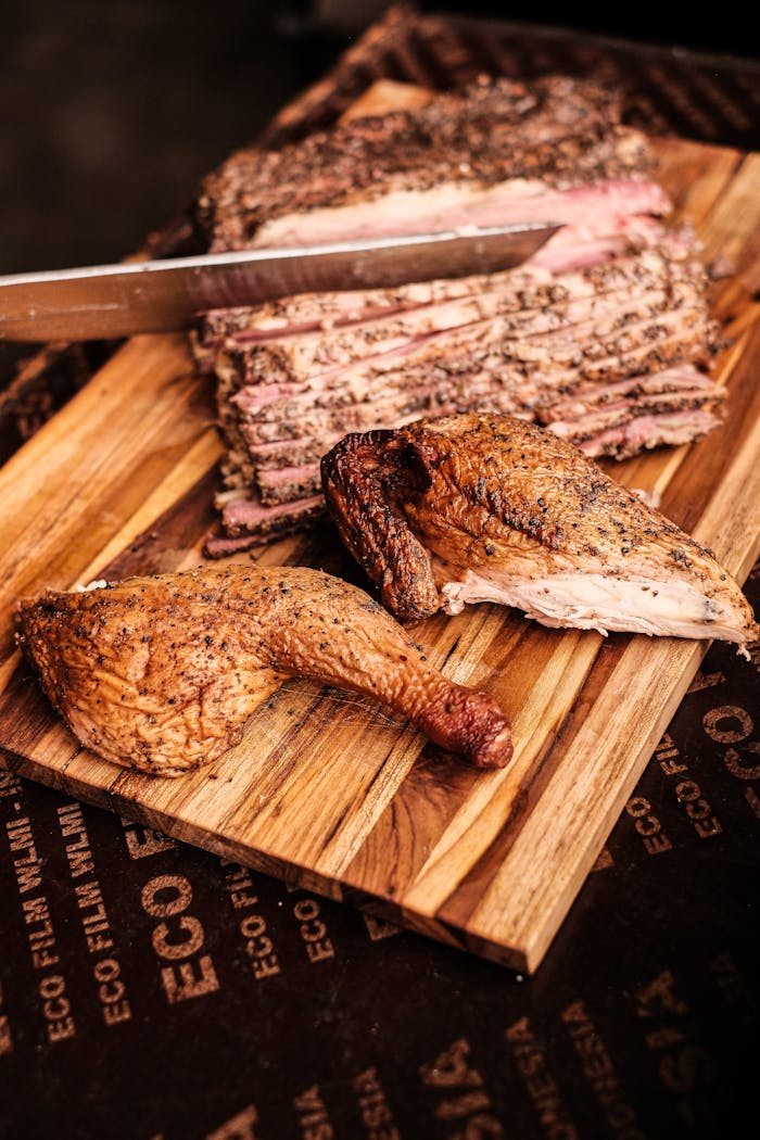Deliciously smoked barbecue brisket and chicken leg on a wooden board, perfect for a savory feast.